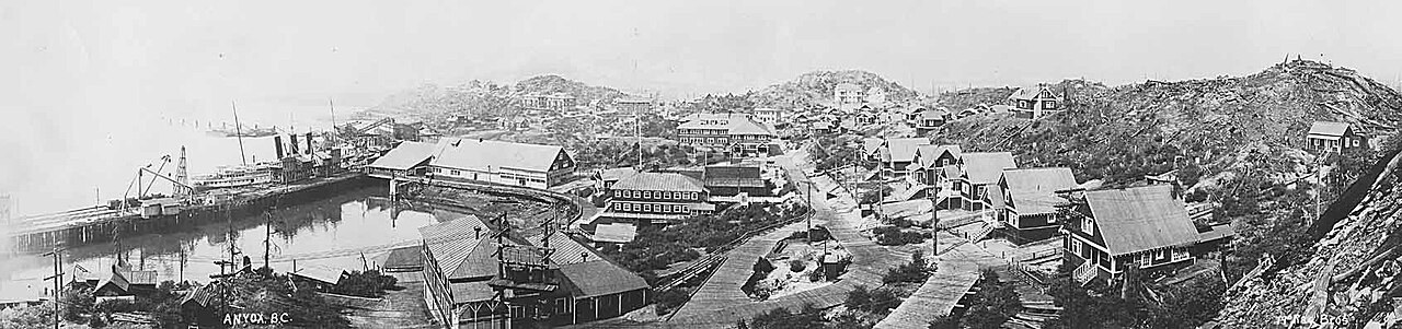 Black-and-white photo of a hillside town of wooden buildings above a waterfront