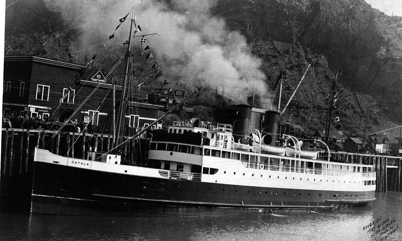 Black-and-white photo of a steamship at a wharf beside buildings