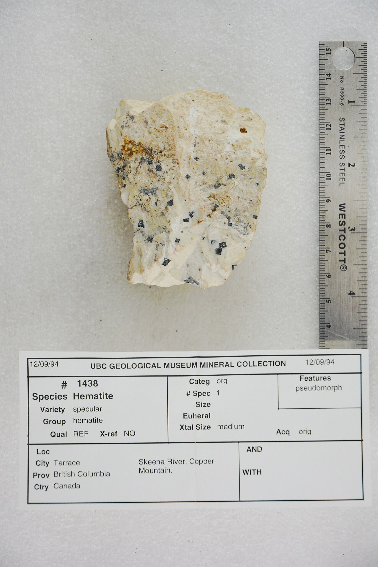 Pale mineral specimen beside a ruler and a museum collection label