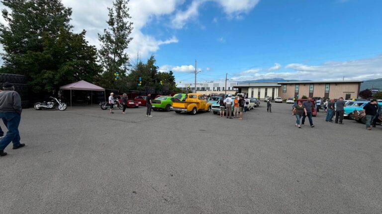 Visitors walk among classic cars and a tent in the parking lot.