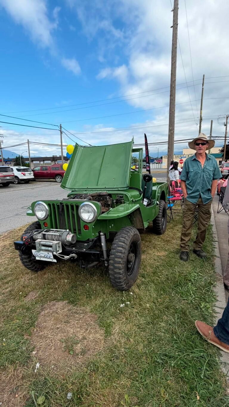 A green vintage Jeep with its hood up and a man standing beside it.