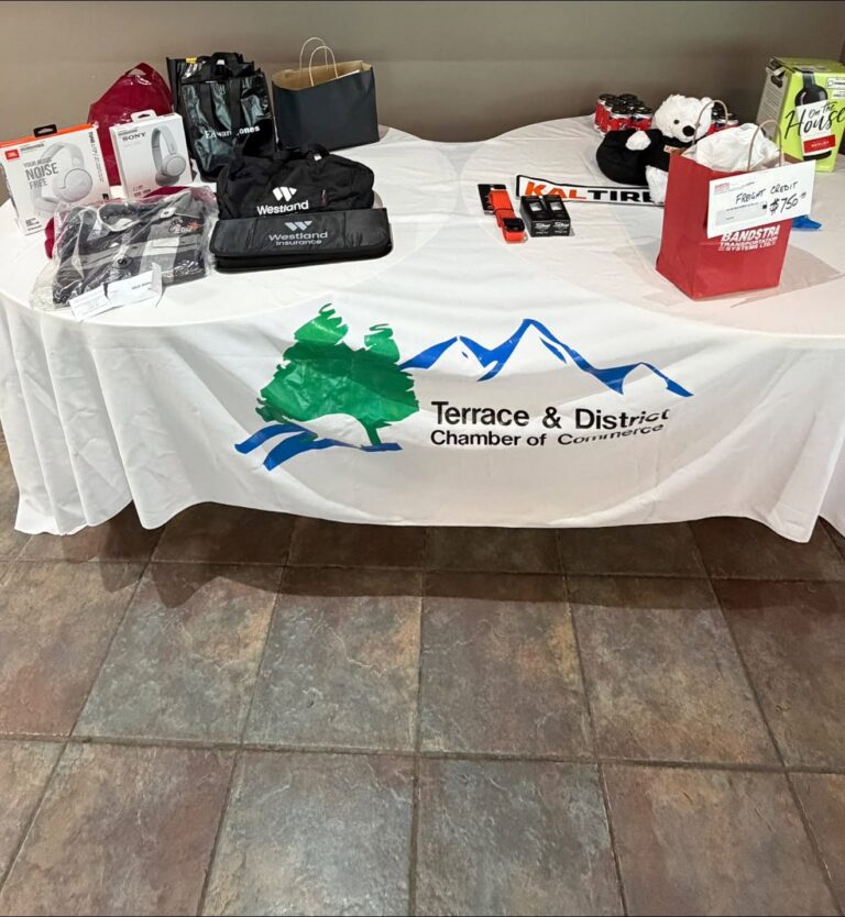 Prize table with gift bags and items on a Terrace & District Chamber of Commerce tablecloth.