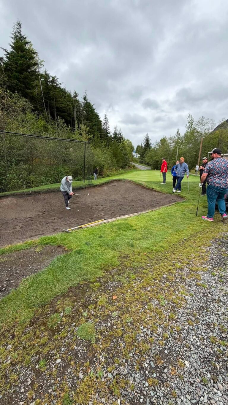 Golfers on a fairway beside a sand bunker under a cloudy sky.