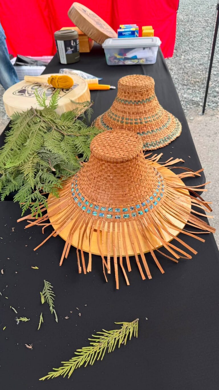 Woven cedar hats and cedar boughs displayed on a table.