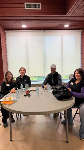 Four attendees seated around a round table by a window at the BC Mining Roadshow in the Terrace Sportsplex.
