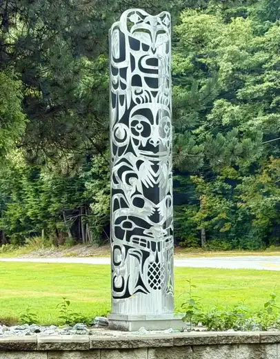 Tall silver and black metal totem-style monument on a lawn at Rio Tinto BC Works.