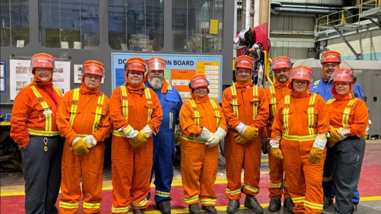 Tour participants in orange and blue safety coveralls, hard hats and safety glasses pose side by side on the plant floor at Rio Tinto BC Works.